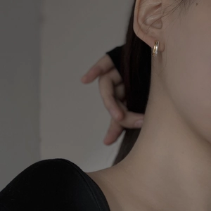 Detail of minimalist two-tone silver and gold hoop earrings on a model's ear