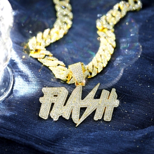 Macro view of gold iced out FLASH letter pendant and Cuban link chain on blue velvet