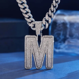 Macro shot of iced-out letter M pendant with diamonds on a thick silver Cuban link chain