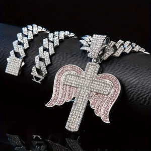 Macro shot of iced out cross pendant with pink angel wings on heavy Cuban link chain