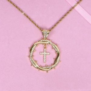 Close-up of golden thorn cross pendant with paved zircons on pink background