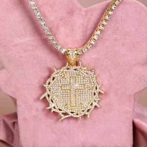 Close-up of golden thorn cross pendant with white zircon stones on pink velvet stand