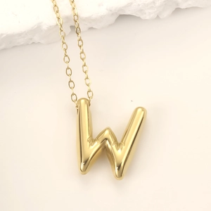 Polished golden stainless steel bubble letter W pendant necklace on a minimalist background