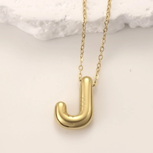 Macro detail of 3D balloon-style golden letter J pendant on a white stone background