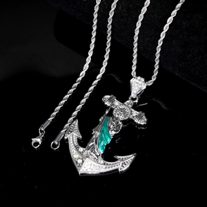 Close-up of iced-out silver anchor cross pendant with green stones and rope chain