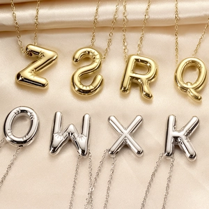 Polished puffy balloon alphabet necklaces in gold and silver on silk background