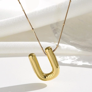 Detail eines goldenen 3D-Buchstaben-U-Anhängers mit glänzendem Finish an einer feinen Kette