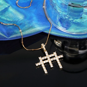 Détail macro du pendentif croix serti de zircons sur chaîne serpent à perles dorées