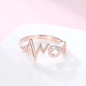 Rose gold infinity and heartbeat ring with shimmering crystals on a white stand