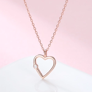 Close-up of rose gold hollow heart pendant with a sparkling zircon on a pink background