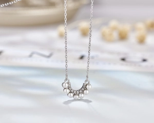 Macro detail of U-shaped silver pendant featuring seven graded pearls and pavé zircons