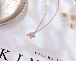 Detail of rose gold clover necklace with sparkling white pavé stones on silk background