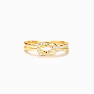 Détail macro de bague nœud dorée avec doubles anneaux entrelacés et pavage de zircons
