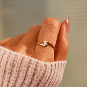Close-up of a minimalist gold S-shaped wrap ring with a single round zircon on a finger