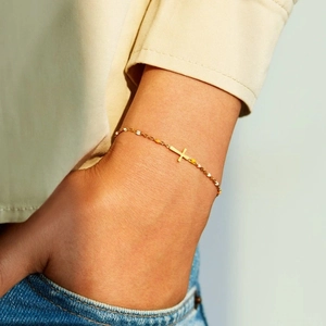 Détail du bracelet croix en argent s925 avec perles en émail jaune et blanc sur chaîne dorée