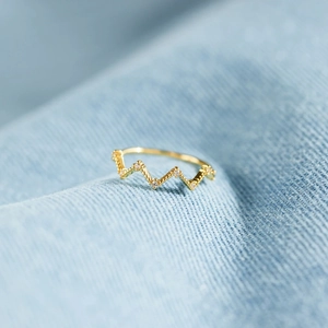 Close-up of gold wavy ring with tiny crystals on a light blue denim background