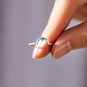 Macro shot of minimalist S925 silver arched ring featuring a delicate round blue gemstone