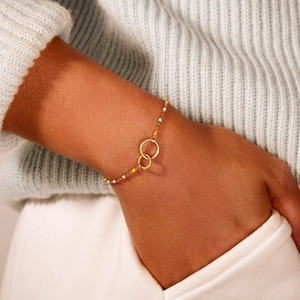Detail of interlocked double rings gold bracelet with colorful beads on female wrist