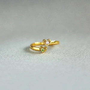 Macro view of gold bypass ring with pink and green heart-shaped gemstones on grey fabric