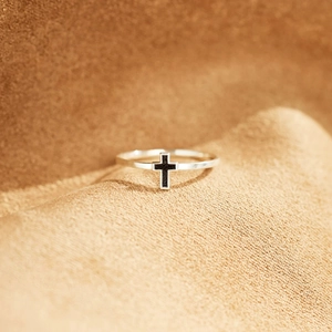 Vue macro d'une bague minimaliste en argent S925 avec croix en émail noir sur tissu tricoté