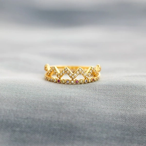 Vue macro d'une bague couronne en argent s925 avec cristaux colorés sur tissu gris