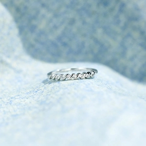 Macro shot of s925 silver twisted ring band with seven inlaid round zircons on blue fabric