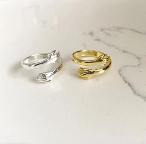 Detail of silver and gold hugging hands open rings on a marble surface