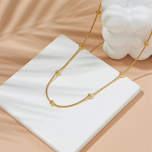 Elegant gold snake chain necklace with bead accents on a minimalist display stand