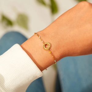 Close-up of a gold chain bracelet with triple interlocking rings and colorful enamel beads