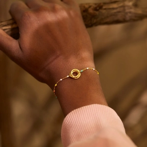 Detail of gold chain bracelet with intertwined rings and colorful enamel beads on wrist
