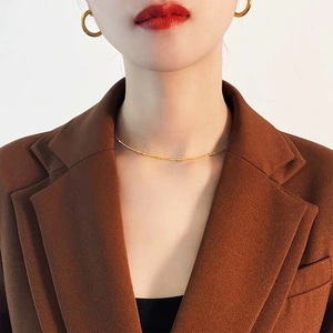 Minimalist 18K gold snake chain necklace with gold beads worn by a model in a suit