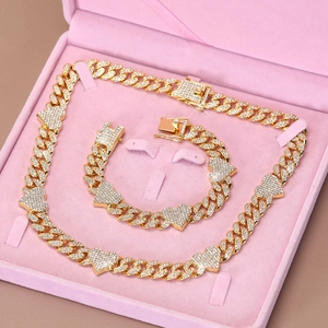 Detail of gold Cuban link jewelry set with iced out heart charms in a pink velvet box