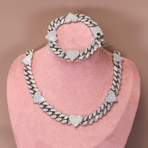 Close-up of Cuban link chain set with pavé-set heart charms on a pink jewelry display