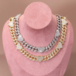 Close-up of gold and silver Cuban link necklaces with diamond-encrusted heart pendants