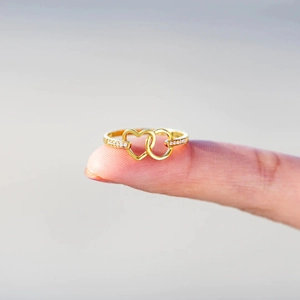 Close-up of interlocking gold heart rings with sparkling zircon inlay on finger