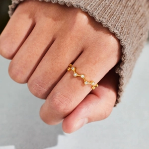 Gros plan d'une bague dorée ondulée avec zircons portée sur une manche en maille