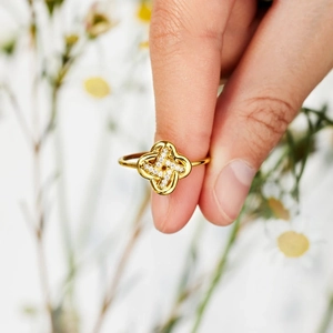 Détail d'une bague trèfle dorée sertie de zircons portée sur la main avec marguerites