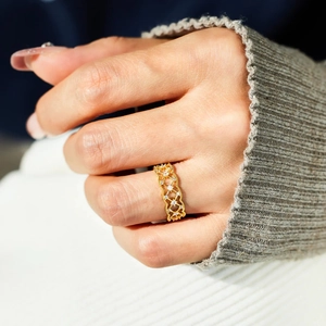 Détail d'une bague quadrillée dorée sertie de zircons portée à l'index