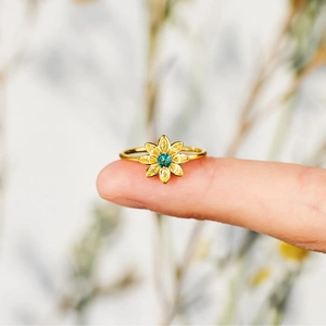 Detailed close-up of a sunflower ring with blue center stone and yellow petals on finger