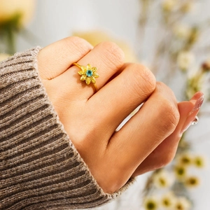 Close-up of a sunflower ring with blue center stone and yellow petals on model finger