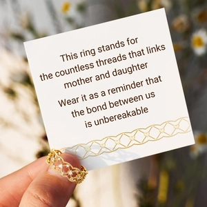 Détail d'une bague tressée dorée avec cristaux tenue contre une carte cadeau mère-fille