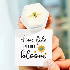 Detailed shot of sunflower ring with blue-green gemstone in white velvet box