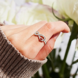 Detail of s925 silver infinity ring with sparkling red heart stone on a soft knit background