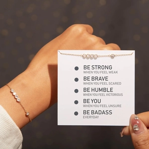 Detail of a thin gold chain bracelet with six round zircons on a white gift message card