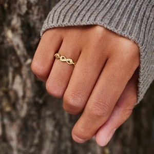Elegant gold infinity loop ring with pavé crystals shown on a natural wood background