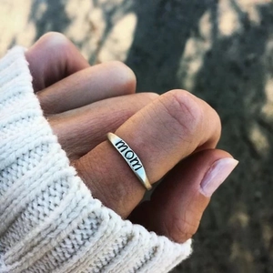 Hand wearing a minimalist S925 sterling silver ring with MOM engraving over a white sweater