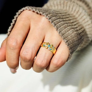Gros plan d'une large bague dorée ornée de pierres multicolores et d'oxydes de zirconium