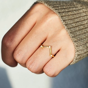 Close-up of a gold V-shaped ring with three white opals on a model's hand