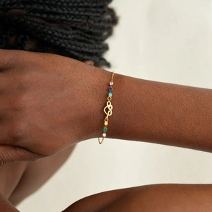 Detail of gold knot bracelet featuring multi-color gemstones on a female wrist