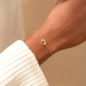 Minimalist gold knot charm bracelet with sleek link chain worn on model wrist